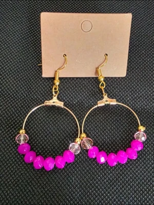 Stora ringörhängen med rosa pärlor - Säljer ett par stora ringörhängen med guldfärgade detaljer och rosa samt genomskinliga pärlor. Örhängena har en modern och trendig look med metallringar och färgstarka pärlor som ger en cool touch till din outfit.
