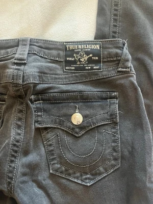 Svarta bootcut jeans True Religion - Säljer ett par svarta jeans från True Religion med bootcut-modell och klassiska kontrastsömmar. Jeansen har två bakfickor med lock och silverfärgade knappar med logga. Materialet är mjukt denim och passformen är relaxed. Modellen heter BECCA mid rise boot 🌟 storleken är W26, innerbenslängden är 82cm 💫