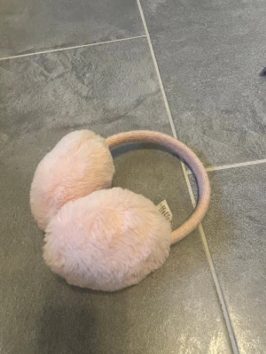 Ljusrosa fluffiga öronmuffar McKinley för barn - Säljer ett par supermjuka och fluffiga öronmuffar för barn i ljusrosa från McKinley. De har stickad båge och stora, gosiga örondelar i fuskpäls. Perfekta för att hålla värmen när det är kallt ute.