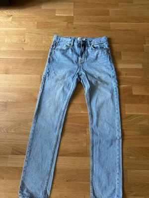 Ljusblå raka jeans - Säljer ett par ljusblå jeans med rak passform och klassisk femficksdesign. Jeansen har normal midja och är tillverkade i denim med en snygg tvätt. Perfekta för en avslappnad och trendig look.