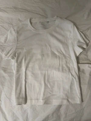 Vit ribbad t-shirt med rund hals - En basic vit t-shirt med ribbad struktur och rund halsringning. T-shirten har korta ärmar och är tillverkad i ett mjukt material som känns skönt mot huden. 