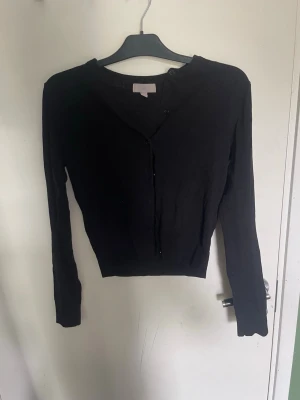 Svart kofta från H&M, storlek S - En klassisk svart kofta från H&M i storlek S. Koftan har långa ärmar, rund halsringning och knäppning framtill. Perfekt att slänga över en topp eller klänning för en enkel och stilren look.
