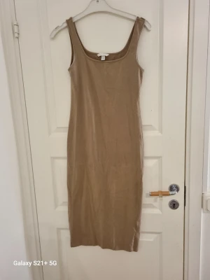 Beige ribbad midiklänning H&M - Snygg beige midiklänning från H&M i ribbad bomullsblandning. Ärmlös med breda axelband och rundad urringning. Perfekt att styla med sneakers eller boots för en trendig look.