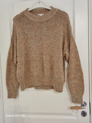 Beige melerad stickad tröja H&M - Stickad tröja från H&M i beige melerad färg med inslag av ljusa toner. Tröjan har rund halsringning, ribbade muddar och avslappnad passform. Perfekt för lager på lager och en chill look.