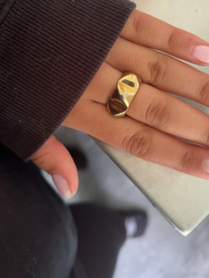 Guldfärgad chunky ring med facettyta - Säljer en snygg guldfärgad ring med chunky design och facettslipad yta som ger en cool och modern look. Ringen är bred och har en blank finish som verkligen sticker ut på fingret. Perfekt för dig som gillar statement-smycken.