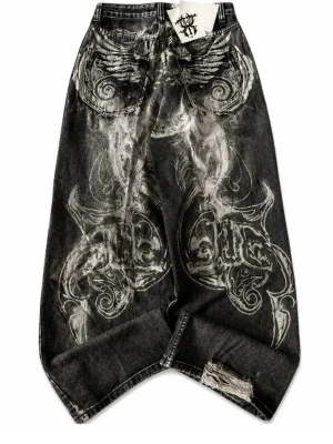 Baggy svarta jeans med tryck - Unika baggy jeans i svart denim med stora vita tribal-inspirerade tryck på bak- och sidopartierna. Jeansen har slitningar vid benslutet och bakfickor med detaljerat mönster. Perfekta för dig som gillar streetwear och vill sticka ut.