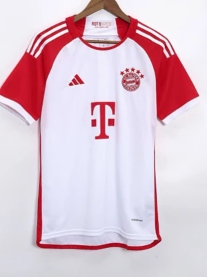 Vit och röd FC Bayern München tröja - Säljer en vit och röd fotbollströja med FC Bayern München-logga och fyra stjärnor på bröstet. Tröjan har röda detaljer på axlar och ärmar, samt Adidas ränder på axlarna. Tillverkad i ett lätt och ventilerande material, perfekt för träning eller match.