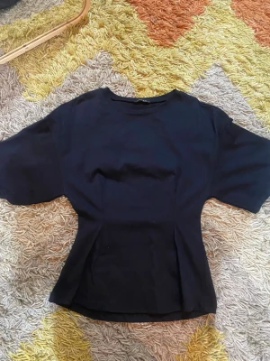 Svart topp från Amisu med vida ärmar - Snygg svart topp från Amisu med rund halsringning och vida korta ärmar. Modellen är figurnära i midjan och har en enkel, stilren design som passar till mycket. Perfekt att matcha med både jeans och kjol för en trendig look.