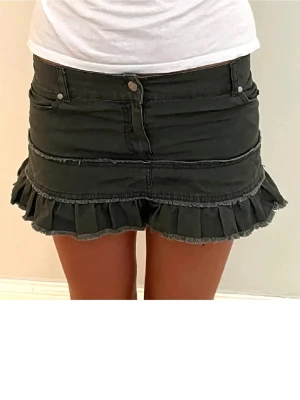Khakigrön volangkjol i denim - Kort grön kjol i denim med volangkant nedtill och råa sömmar. Kjolen har klassisk femficksmodell och knappgylf. Perfekt för dig som gillar en edgy och trendig stil. Alla bilderna är mina jag är 165 och skulle säga att det är en storlek s💕är från ett märke som heter jny Jennifer 