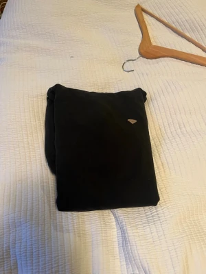 Svart hoodie med magficka från blend  - En svart hoodie med klassisk magficka och ribbade muddar. Tröjan har en liten diskret logga på bröstet och är tillverkad i mjukt material, perfekt för chill dagar. Passar dig som gillar enkel och stilren streetwear.