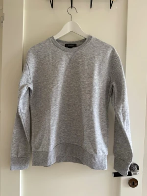 Ljusgrå sweatshirt  - En basic ljusgrå sweatshirt i mjukt material. Tröjan har rund halsringning, långa ärmar och ribbade muddar vid ärmslut och nederkant. Enkel och stilren design utan tryck eller detaljer, perfekt för en avslappnad look. Använd en gång. Rökfritt hem. Kolla gärna in mina andra annonser.