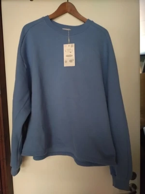 Blå sweatshirt i storlek L - Säljer en stilren blå sweatshirt i storlek L. Tröjan har rund halsringning, långa ärmar och ribbade muddar vid ärmslut och nederkant. Perfekt för en avslappnad och enkel look. Materialet känns mjukt och bekvämt mot huden. Aldrig använd, prislapp sitter på. 