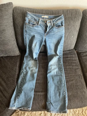 Ljusblå bootcut jeans från Levi's - Säljer ett par ljusblå Levi's jeans med klassisk femficksdesign och bootcut passform. Jeansen har normal midja, dragkedjegylf och Levi's ikoniska läderpatch bak i linningen. Perfekta för en avslappnad och trendig look. Bakom benet finns en fläck som dessvärre inte går bort men den är liten.