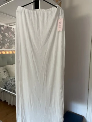 Vit långkjol från Nelly - Säljer en vit långkjol som jag inte fått användning av då jag har en annan som jag tycker om bättre😊den är helt oanvänd med lapp kvar, sista bilden visar jag hur tyget ser ut då den är en aning genomskinlig💕