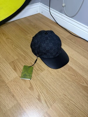 Svart keps med GG-mönster - Snygg svart keps med klassiskt GG-mönster över hela kepsen och en stilren böjd skärm i svart läder. Perfekt accessoar för att lyfta din streetwear-look. Kepsen har justerbar passform och tydlig logga. Helt ny