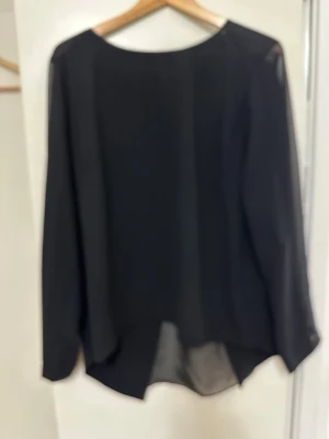 Svart transparent blus med slits bak - Snygg svart blus i transparent material med lång ärm och rund halsringning. Blusen har en unik slitsdetalj baktill som ger en cool look. Perfekt att styla med jeans eller kjol för en trendig outfit.