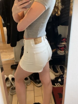 Vita högmidjade jeansshorts - Säljer ett par vita högmidjade jeansshorts med råa kanter och klassisk femficksdesign. Shortsen har knapp- och dragkedjestängning.