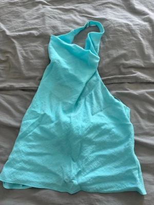 Turkos ärmlös linnetopp - Snygg turkos linnetopp med halterneck och öppen rygg. Toppen är ärmlös och har en lätt och luftig känsla, perfekt för varma dagar. Enkel och stilren design som passar till många olika outfits.