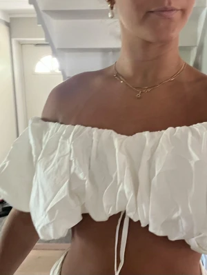 Vit offshoulder croppad topp - Säljer en vit offshoulder topp med puffiga ärmar och croppad passform. Toppen har en dragsko i midjan för justerbar passform och är tillverkad i ett lätt bomullsliknande material. Perfekt för sommarens alla tillfällen!