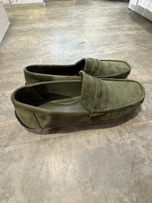 Olivgröna mockaloafers - Snygga loafers i olivgrön mocka med klassisk pennyloafers-design och rundad tå. Skorna har diskreta sömmar och en stilren look som passar till många outfits. Perfekta för dig som gillar en avslappnad men ändå trendig stil.