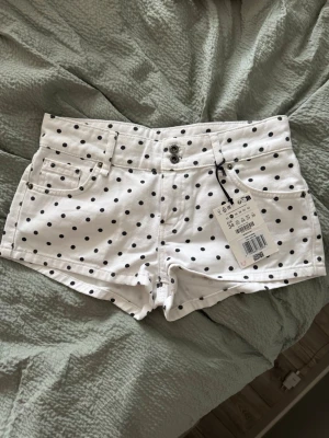 Vita prickiga shorts - Snygga vita shorts med svarta prickar och låg midja. Klassisk femficksmodell med dubbla knappar och dragkedja framtill. Perfekta för sommaren och ger en fräsch look till alla outfits.