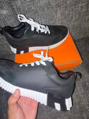 Svarta sneakers med vit sula - Säljer ett par svarta sneakers med chunky, räfflad vit sula och svarta detaljer. Skorna har vita skosnören och ovandel i en mix av mocka och syntetmaterial. Snygg kontrast mellan svart och vitt gör dem riktigt stilrena och moderna.