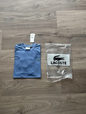 Blå Lacoste t-shirt i bomull - Säljer en stilren blå t-shirt från Lacoste med klassisk krokodillogga på bröstet. T-shirten har rund hals, korta ärmar och är gjord i mjuk bomull. Perfekt för dig som gillar enkel och snygg design.