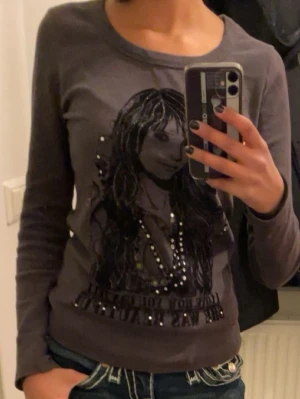 Mörkgrå långärmad topp med tryck - Snygg mörkgrå långärmad topp med ett stort tryck av en tjej på framsidan och texten 'I love how you can tell she was beautiful'. Dekorerad med små pärlor som ger extra detalj. Jag köpte den från en archive secondhand affär i london, älskar tröjan men säljer för den inte passar mig längre. 