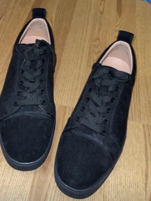 Svarta loubutin sneakers i mocka-look - Stilrena svarta sneakers med mocka-liknande material och svarta skosnören. Klassisk låg modell med rund tå och diskret design. Passar perfekt till jeans eller streetwear.