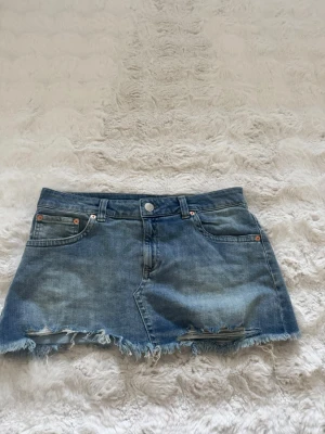 Blå jeanskjol  - Snygg blå jeanskjol i kort modell med fransig, rå kant nertill. Från Nelly
