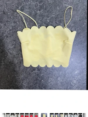Gul scallop crop top med tunna band - Söt gul crop top med scallop-kant upptill och nedtill samt tunna axelband. Toppen har en enkel, rak passform och är gjord i ett mjukt, stretchigt material som känns bekvämt mot huden. Perfekt för sommardagar eller festivaler.