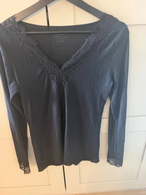 Svart långärmad topp med spets - Snygg svart långärmad topp från Intimissimi med v-ringning och spetsdetaljer vid halsringning och ärmslut. Tillverkad i ett mjukt material med inslag av kashmir som känns lyxigt mot huden. Perfekt för dig som vill ha en stilren men ändå feminin look. Är i storlek m med passar mig som vanligtvis har storlek S 