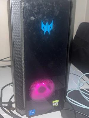 Acer Predator stationär gamingdator - Säljer en svart Acer Predator stationär dator med glasfront och RGB-belysning. Chassit har en modern design med Predator-logga i blått, synlig kylfläkt med rosa ljus och sidopanel i metall med grönt ljus. Utrustad med Intel Core i5 och NVIDIA GeForce RTX 3070ti