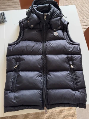 Moncler väst - Säljer nu min dunväst med luva ifrån Moncler. Den är inte använd alls ltxbrt och i riktigt fint skick. Den kan användas på vintern också, perfekt för lager på lager och håller dig varm under kyliga dagar.