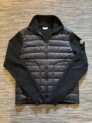 Svart Moncler cardigan - Säljer en snygg cardigan från Moncler! Cardiganen är i mycket bra skick och har inga defekter förutom att nacklappen sitter lite löst. Qr-kod och nfc-scan på armen funkar som dem ska. Om ni har några frågor så hör av er😊