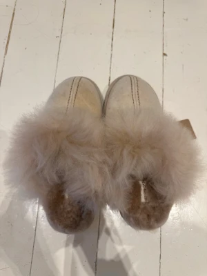 Beige fårskinnstofflor Shepherd - Beige tofflor från Shepherd i äkta fårskinn med fluffig ullkant. Aldrig använda då dom var för små. Fick i present av släkting. Ordinariepris 1100kr.
