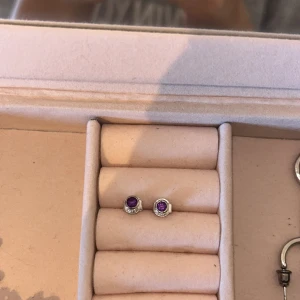 Örhängen med lila sten och örhängen med klar sten - Ett par örhängen med amatist kristall. Örhängena är i silverfärg och har en enkel, elegant design. De lila stenarna är infattade i en silverram och örhängena har en stämpel med '925', vilket indikerar att de är gjorda av sterlingsilver. Helt oanvända då jag inte tåler dom. 