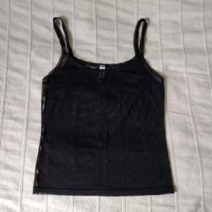 Svart see through linne med spets - genomskinlig topp i mesh - Stretchigt see through/genomskinligt linne/topp med spets. Meshliknande tyg. Storlek M. 86% polyamid och 14% elastan. I fint skick.