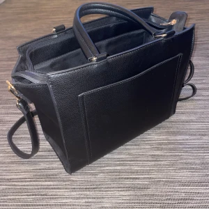 Handväska  - Svart handväska från about you.   30 cm lång  22 cm djup  10 cm bred.  Två fack inuti väskan som delas med ett tygfack i mitten med dragkedja på. 