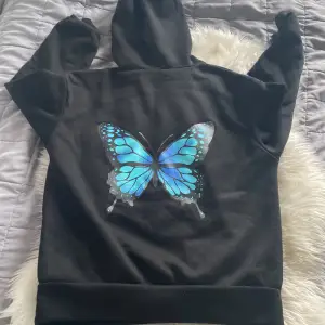 en svart hoodie me en blå fjäril där bak använd i bra skick
