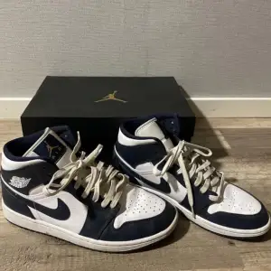 Väldigt fina Air Jordan 1 Mid i färgen white/metallic gold-obsidian som är i väldigt bra skick. Nästan aldrig använda, kommer även med lådan som jag fick dem i och ett par helt nya svarta skosnören. Hör av dig om du blir intresserad