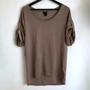 Brun stickad t-shirt i ull, stl XS, kortärmad topp, mullvad, bohemisk, boho - Brun stickad topp i ullblandning, upprullade ärmar med justerbara hällor, längre bak, lätt lyster, något nedhasad axel. Visst ytslitage finns. Mått i cm: bröstvidd 47; längd fram från axeln 67.