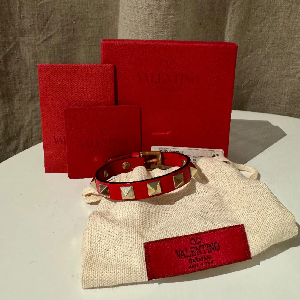 Rött valentino armband med guldiga nitar. Endast använt vid speciella tillfällen så fortfarande i väldigt fint skick. Originallådan med tillhörande lappar finns kvar. . Accessoarer.