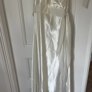 Vit klänning - En till vit klänning i gräddvit med band runt midjan, dold dragkedja och öppen rygg. Använd en gång men det finns en liten smuts enligt bilden som går bort i tvätt. Jag har aldrig tvättat den.