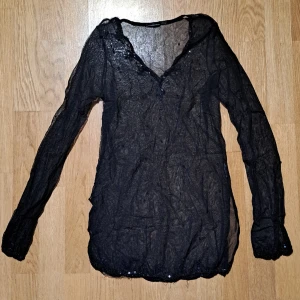 Svart mesh tröja - Svart långärmad tröja i mesh. Paljetter och pärlor vid kragen, ärmsluten och fållen. Köpt på secondhand, men den är lite för liten så har inte kommit till användning. Finns ingen lapp så vet inte märke eller storlek, men är ca en xs-s.