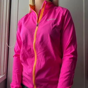 Rosa träningsjacka - Säljer nu denna tröningsjacka då den inte kommer till användning längre. Tröjan är andrahand men jag själv har inte använt den många gånger. Jättetunn och skön att ha utomhus när det är lite mitt-i-mellan-väder. Superbra ficka för plånbok mm på ryggen!!💗