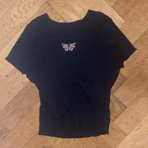 En croppad svart t-shirt med en broderad fjäril på bröstet. Frakt ingår inte i priset men priset kan diskuteras, om ni har frågor så skriv🫶