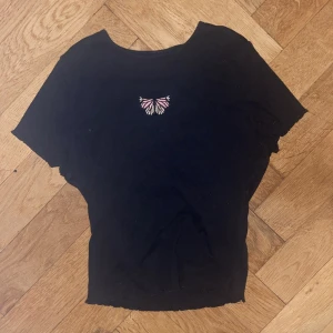 Liten t-shirt med fjäril - En croppad svart t-shirt med en broderad fjäril på bröstet. Frakt ingår inte i priset men priset kan diskuteras, om ni har frågor så skriv🫶