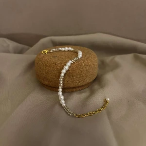 Armband - Thimea - Beskrivning: Detta armband heter Thimea och är ett armband med olika storlekar av vita pärlor och beiga pärlor med lås och kedja i guldplätering. Namn: Thimea Längd: Hela 22,5 cm Pärlor 15 cm 