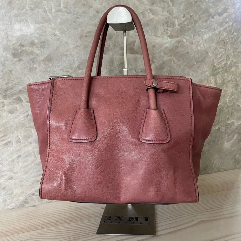 Prada Tote Bag  All traces of use can be seen in the pictures. I can send more pictures if it needs   Width: 26 (bottom) - 36 (top) cm Height: 21 cm Depth: 15 cm Handle drop: 13 cm Colour: Pink Material: Leather Included: Dustbag and authenticity car. Väskor.